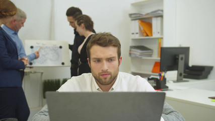 Man working at the laptop, his workmates discuss scheme of apartement 