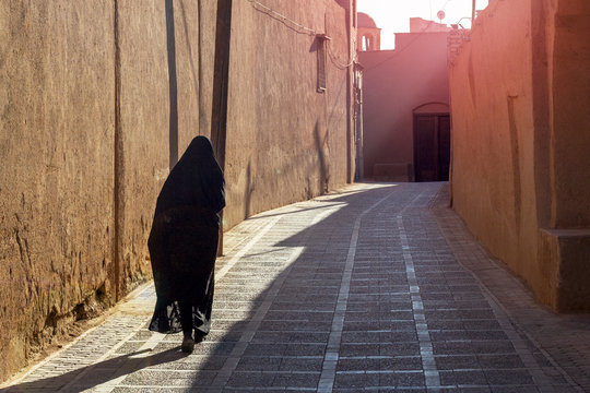 A woman in traditional black Islamic clothing walks the empty morning street of the eastern city. Back view.