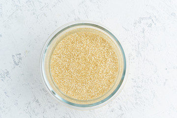Soaking quinoa cereal in water to ferment cereals and neutralize phytic acid. Large glass bowl with grains flooded with water. Top view, close up, white background