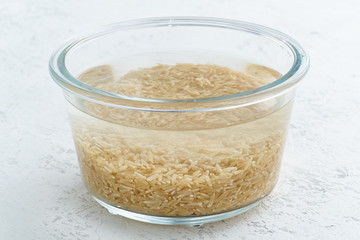 Soaking brown rice cereal in water to ferment cereals and neutralize phytic acid. Large glass bowl with grains flooded with water. Side view, close up, white background
