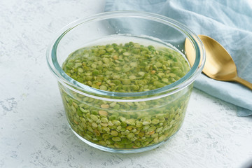 Soaking green peas cereal in water to ferment cereals and neutralize phytic acid. Large glass bowl with grains flooded with water. Side view, close up, white background