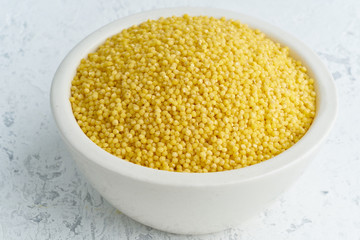 Millet, bulrush in white bowl on white background. Lectine free, dried cereals in cup, vegan food, fodmap diet. Side view, close up.