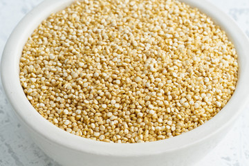 Quinoa seed in white bowl on white background. Dried cereals in cup, vegan food, fodmap diet. Side view, close up.