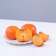 Fresh beautiful sliced sweet persimmon kaki isolated on white kitchen table with gray blue background, Chinese lunar new year design concept, close up.