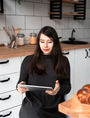 A young woman in the kitchen is looking at something on a tablet. Modern white kitchen.