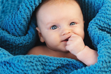 A cute baby boy wrapped in a cosy blue blanket looking at the camera