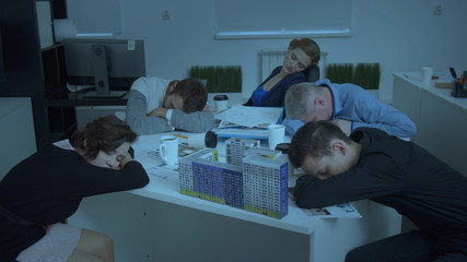 Model of house on table, workmates sit and sleep