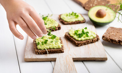 Girl decorating rye bread sandwiches with avocado spread