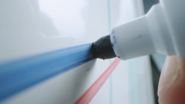 Macro Follow Shot of a Blue Marker Pen Being Held with a Hand. Person Drawing Graphs on a Whiteboard and Inserting a Tick Mark. Pencil is Connected to the Camera. Gripped Shot.