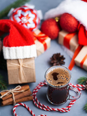 Christmas composition with gift boxes in Santa hat and a glass of coffee on the holiday table