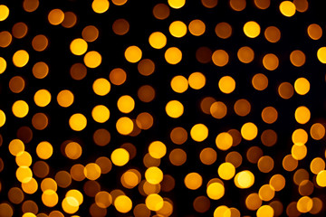 Bright light of orange burning lanterns bokeh from a garland in defocus at night against a dark background © Aleksey Vlasenko