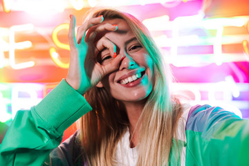 Image of blonde woman showing ok sign over multicolored neon text sign