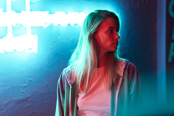 Image of young woman standing over multicolored neon text sign outdoors