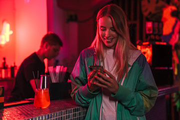 Image of woman holding smartphone in bar over neon lightening