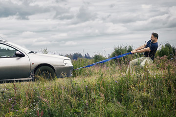 Middle-aged man pulls his car which has run out of petrol along a country road using a tow rope....