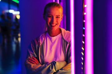 Image of young woman standing by multicolored neon illumination indoors