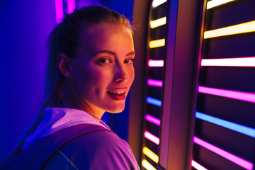 Image of young woman standing by multicolored neon illumination indoors