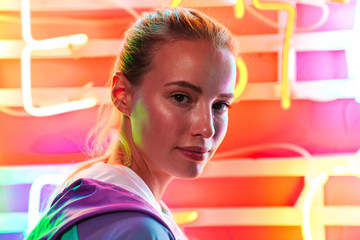 Image closeup of young woman standing over multicolored neon text sign