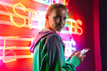 Image of beautiful woman holding smartphone over neon text sign