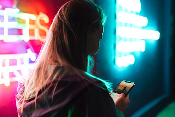 Image of beautiful woman holding smartphone over neon text sign