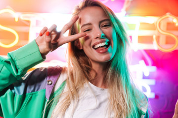 Image of woman showing peace fingers over multicolored neon text sign