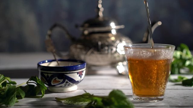 Cinemagraph of closeup of tea pouring into a glass with Moroccan tea set and mint.