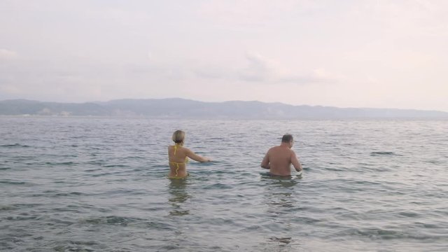 Married couple swimming in sea on background of mountains. woman in yellow bikini goes into sea water.