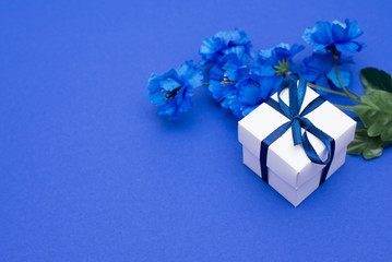 Bouquet of flowers and gift box on classic blue background, top view, space for text, flat lay