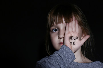 Abused little girl showing palm with phrase HELP ME on black background, space for text. Domestic...