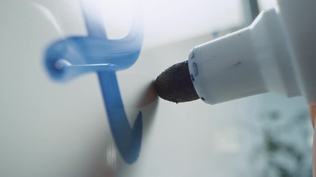 Macro Follow Shot of a Blue Marker Pen Being Held with a Hand. Teacher Writing on a Whiteboard with Mathematical Formulas and Business Plans. Pencil is Connected to the Camera. Gripped Shot.