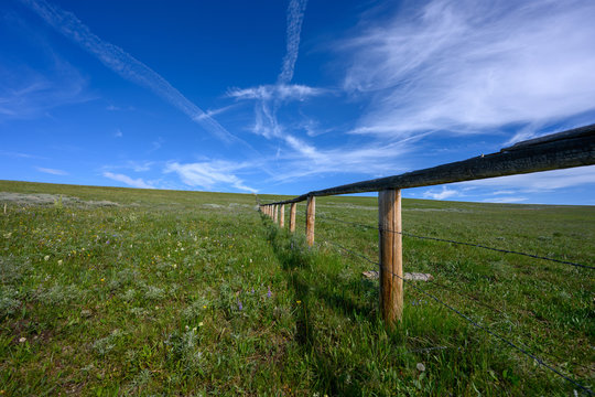 Low Angle of Wooden Fence with barbed Wire Across Green Field