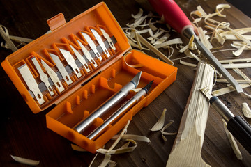 An open set of knives with interchangeable nozzles for carving wood and a chisel with a red handle on the table.
