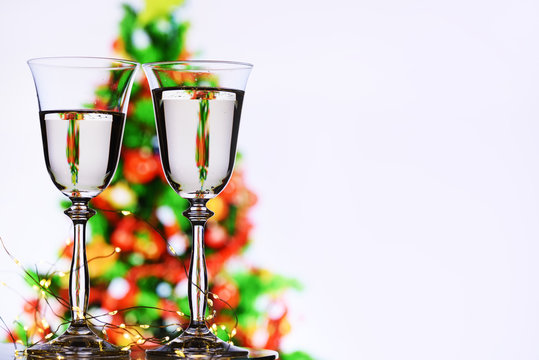 Two glasses of champagne with sparkling wine and a blurred image of a Christmas tree on a white background with reflection of a Christmas tree in a glass. free space for your inscriptions.
