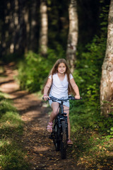 Fototapeta na wymiar Cute little teenager girl riding bicycle in a sunny park