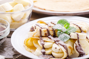 French crepes with chocolate sauce and banana in ceramic dish on wooden kitchen table