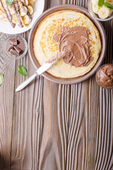 Flat lay French crepes with chocolate sauce and banana in clay bowl on wooden kitchen table