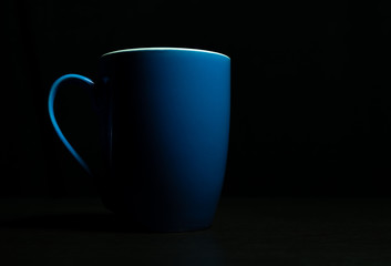 Low light view and copy space. Blue ceramic cup some light hits the surface placed on the dark shadows.
