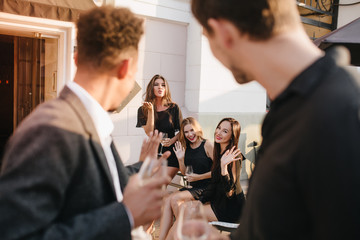 Close-up portrait from back of european brunette man looking at cute girls sitting beside restaurant. Outdoor photo of guys going to getting acquainted with ladies.