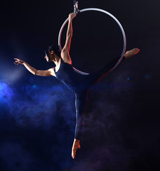 Young woman performing acrobatic element on aerial ring against dark background © New Africa