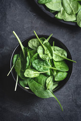 Fresh spinach leaves in the blacl blowl on a dark textured background