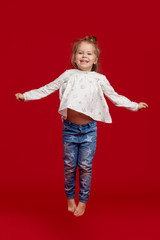 Happy childhood. Funny child girl jumping and having fun isolated on red background. Celebrating a vibrant carnival for kids, birthday party. True emotions. Space for text