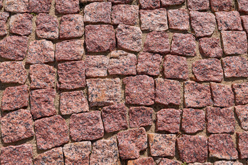 A sidewalk or path paved with a mosaic of square cobblestones or stones. Cobblestones lie on the sand. Grid or matrix of square shapes. The stones are red-brown with dark specks. Background, backdrop.