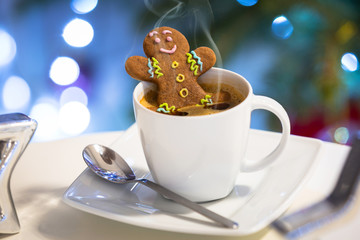 Gingerbread cookie man takes a bath in the cup of hot coffee with christmas background
