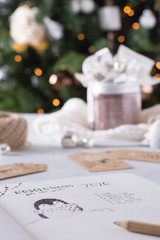 Resolutions for the new year 2020 - Man writing by hand a goals list for the new year on a notebook while enjoying christmas lights and christmas atmosphere. Change and inspirational concepts.