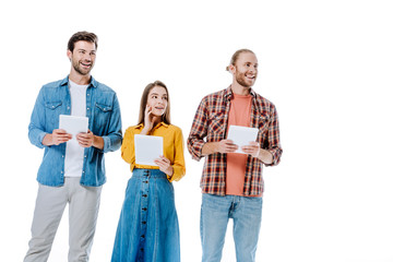 smiling three young friends holding digital tablets and looking away isolated on white