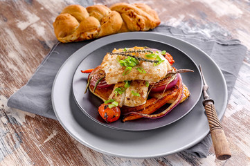 Appetizing cod filet with red onion and herbs, baked potatoes and carrots on a side dish in a gray plate on a napkin. Tasty and healthy seafood