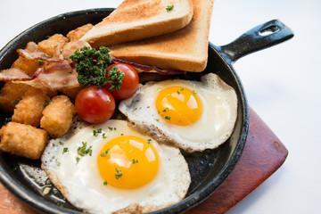 Close up image of sunny side up egg skillet on a black background and wooden plate,