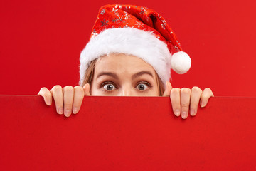 Shocked surprised girl in santa claus hat isolated on festive red background with copy space, time...