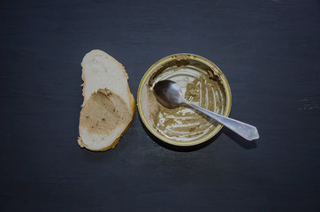tin can with fish paste on a black background and a slice of bread. View from above.