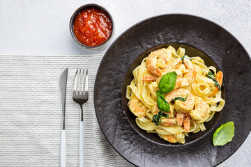Italian pasta fettuccine in a creamy sauce with shrimp on a black plate, top view